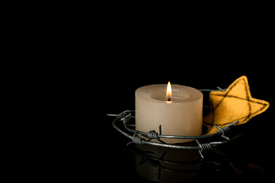 Burning candle with barbed wire and Jewish badge on dark background. International Holocaust Remembrance Day