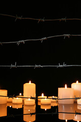 Barbed wire and burning candles on glass table against dark background. International Holocaust...