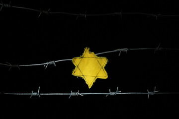 Barbed wire with yellow Jewish badge on dark background. International Holocaust Remembrance Day