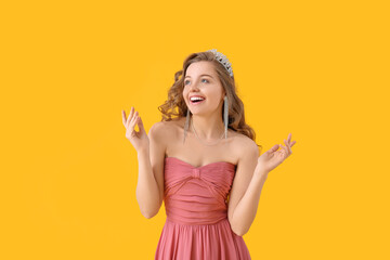 Happy young woman in tiara and prom dress on yellow background - obrazy, fototapety, plakaty