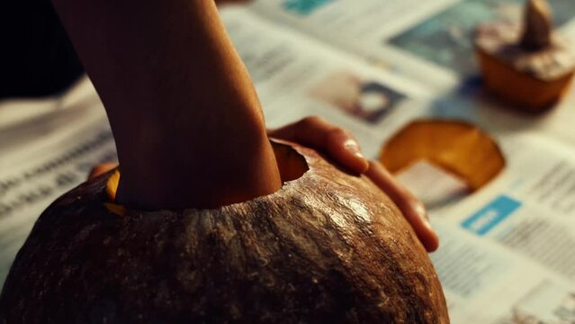 Hands preparing a Halloween pumpkin. Small hand digs inside the pumpkin and removes the seeds. Fingers carve a large orange pumpkin and remove the mush from the inside.