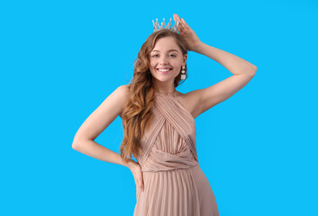 Young woman in crown and prom dress on blue background © Pixel-Shot
