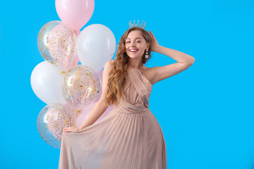 Young woman in crown and prom dress with balloons on blue background © Pixel-Shot