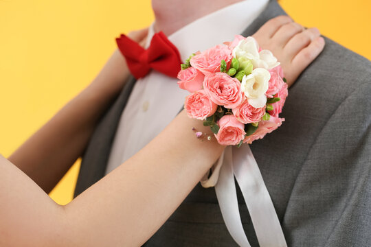 Young woman with corsage hugging her prom date on yellow background, closeup