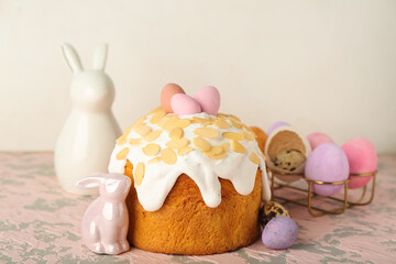Easter cake, painted eggs and bunnies on table near white wall