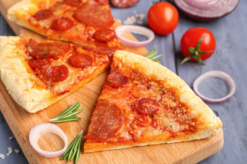 Board with slices of delicious pepperoni pizza and ingredients on blue wooden background