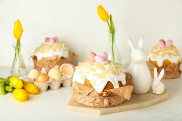 Fototapeta na wymiar Easter cakes with painted eggs, tulip flowers and bunnies on table near white wall