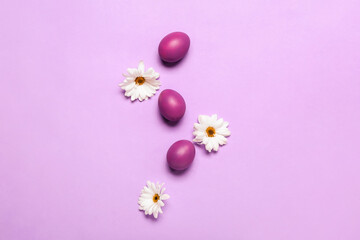 Composition with painted Easter eggs and chamomile flowers on lilac background