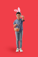 African-American little boy in bunny ears with basket of Easter eggs on red background