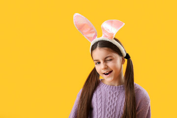 Little girl in bunny ears winking on yellow background