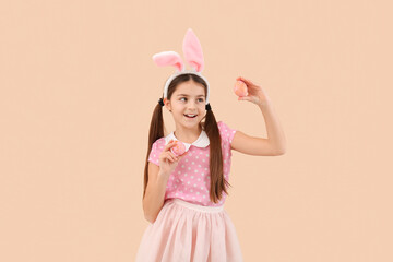Little girl in bunny ears with Easter eggs on beige background
