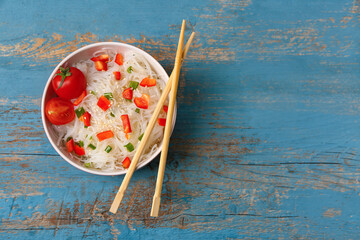 Bowl of tasty rice noodles with vegetables on color wooden background