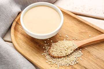 Board with bowl of tasty tahini and sesame seeds, closeup