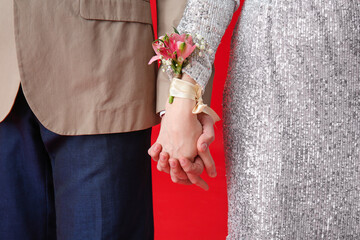 Young girl and her prom date holding hands on red background, closeup