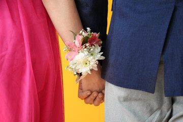 Young girl and her prom date holding hands on yellow background, closeup