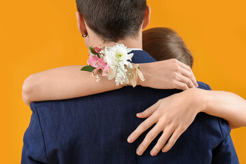 Young girl with corsage hugging her prom date on yellow background - obrazy, fototapety, plakaty