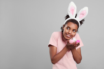 Happy African American woman in bunny ears headband with Easter egg on gray background. Space for text