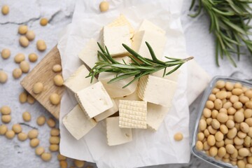 Fototapeta na wymiar Delicious tofu cheese, rosemary and soybeans on light gray textured table, flat lay