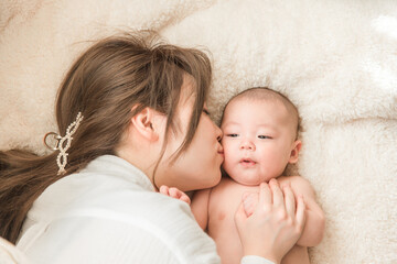 布団の上でリラックスする赤ちゃんと産後のママ（親子・出産・母子・産後・産褥期）
