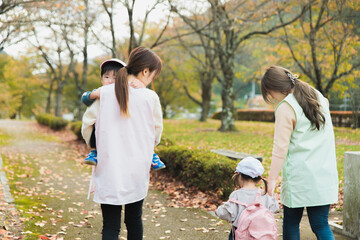 秋の公園を散歩・遠足する保育士の女性と園児（保育園・幼稚園保母）
