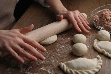 Fototapeta premium Woman rolling dough for chebureki on wooden table, closeup