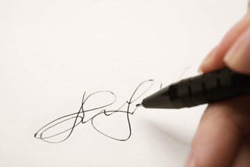 Woman writing her signature with pen on sheet of white paper, closeup - obrazy, fototapety, plakaty