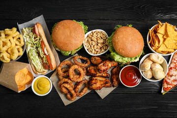 Burgers, onion rings and other fast food on black wooden table, flat lay