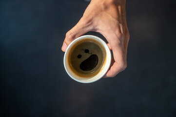 Black coffee in a paper cup with an artistic smiley face on a black table at a coffee shop.