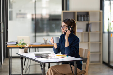 Cheerful business Asian woman freelancer making telephone call share good news about project working in office workplace, business finance concept.	