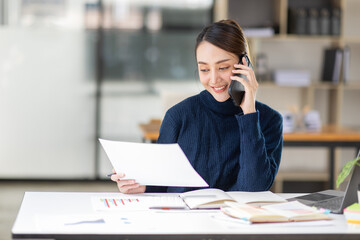 Cheerful business Asian woman freelancer making telephone call share good news about project working in office workplace, business finance concept.	