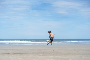 garoto controlando a bola de futebol na praia vazia 