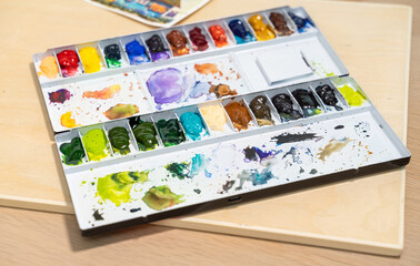Colorful watercolor palette on table with watercolor set. Selective focus.