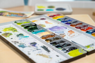 Colorful watercolor palette on table with watercolor set. Selective focus.