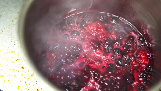 Close-up shot of berries boiling in a metal pot making compote
