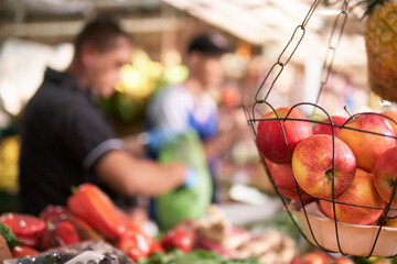 basket of red apples in foreground with two unrecognizable out-of-focus men in the background of fruit stand