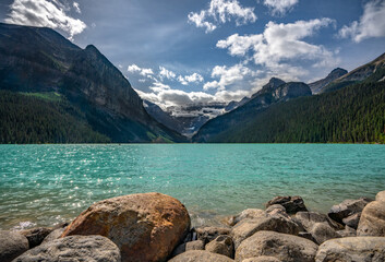 Stunning Lake Louise view with rocks in foreground and Rocky Mountain landscape.