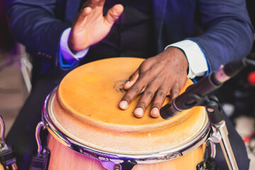 Bongo drummer percussionist performing on a stage with conga drums set kit during jazz rock show performance, tumbadora quinto with latin cuban afro-cuban jazz band performing in the background