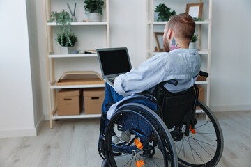 A man in a wheelchair freelancer works at a laptop at home, restriction of movement, view from the...