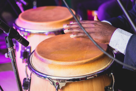 Bongo drummer percussionist performing on a stage with conga drums set kit during jazz rock show performance, tumbadora quinto with latin cuban afro-cuban jazz band performing in the background