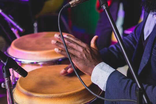 Bongo drummer percussionist performing on a stage with conga drums set kit during jazz rock show performance, tumbadora quinto with latin cuban afro-cuban jazz band performing in the background