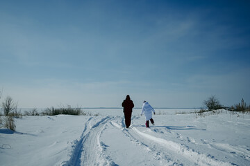 A girl and a man walk on a stitch on a winter day and look into the distance. A woman in a white coat, a man in a black jacket on the winter coast. A cold day.