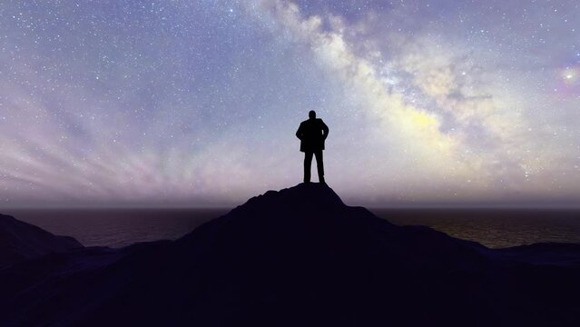 Silhouette of a man standing on the top of the mountain at night looking at the starry sky and imagining the future.