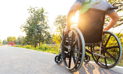 Disability man sitting on wheelchair  in public park with sunray and light.His hand holding the wheel control.Selective focus at front wheel.Wheelchair for elderly with orthopedic problem.Copy space.