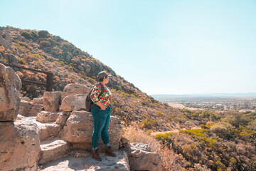 young adult woman in a flowered shirt looking at the landscape from the top on a mountain at sunset