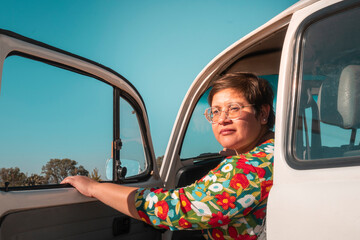 Naklejka premium female traveler looking back with open door of her classic car at sunset