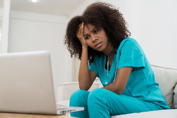 Stressed female doctor with hand on forehead while working with laptop computer in hospital....