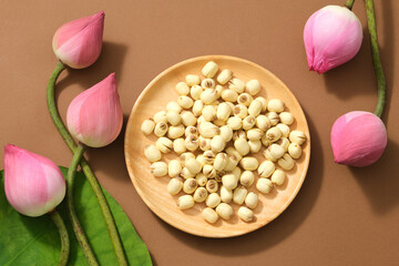 Top view of (Nelumbo nucifera) fresh lotus buds, green leaf and lotus seeds on wooden dish on brown background. Lotus flower is the Vietnamese national flower.