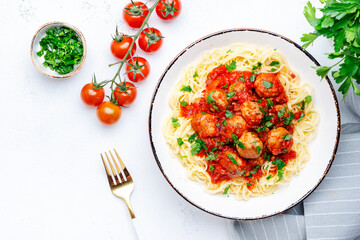 Spaghetti pasta with meatballs in spicy tomato sauce with parsley in plate, white table background, top view