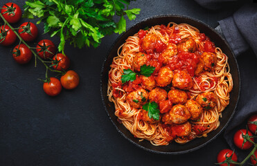 Spaghetti pasta with meatballs in tomato sauce with parsley in frying pan, dark table background, top view