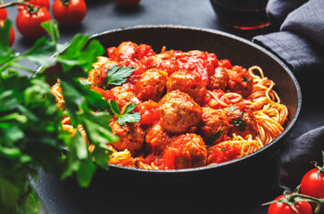 Spaghetti pasta with meatballs in tomato sauce with parsley in frying pan with sangiovese red wine, dark table background, top view